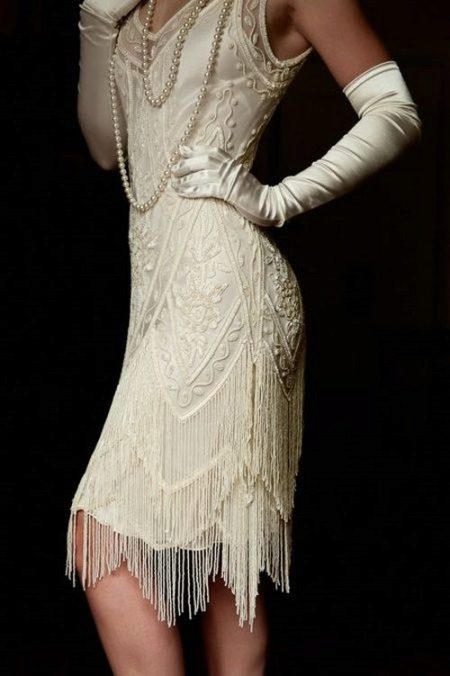 White dress with an asymmetrical bottom of the skirt in the style of Gatsby in combination with gloves and pearls
